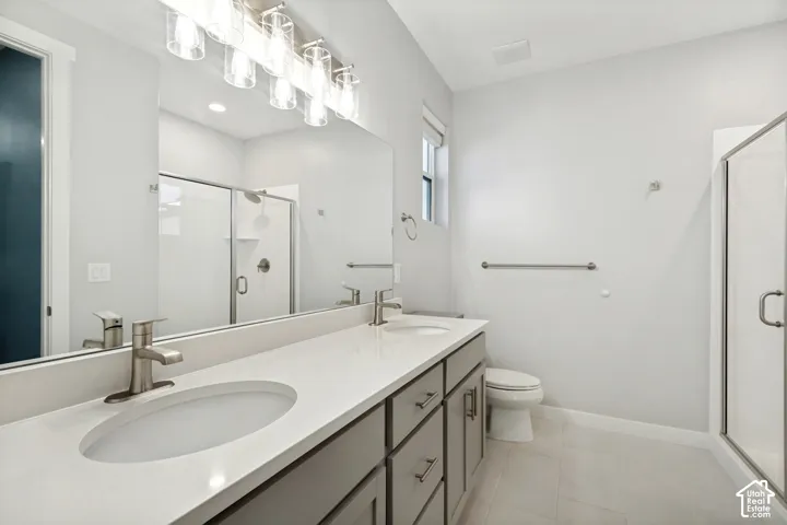 Dual vanity with integrated sinks and brushed nickel faucets, quartz-finish countertop, full-width mirror, overhead vanity lighting, and glass-enclosed shower