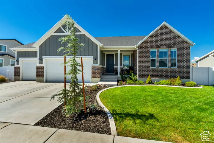 Brick and siding exterior featuring a covered entry, concrete driveway, three-car garage, and a manicured lawn with landscape curbing