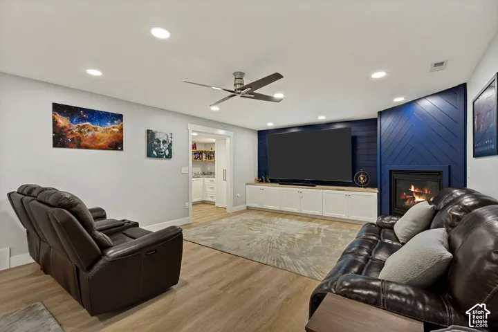 Recessed lighting throughout, LVP flooring, built-in media console with storage, modern fireplace with blue paneling, and a ceiling fan