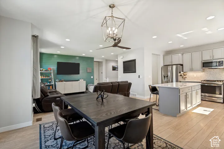 LVP flooring throughout, kitchen with light gray cabinetry and stainless steel appliances, central kitchen island with seating, recessed lighting, and a modern ceiling fan with integrated lighting