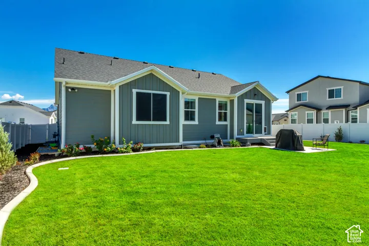 Expansive backyard featuring a manicured lawn, established landscaping, and a patio with a concrete pad