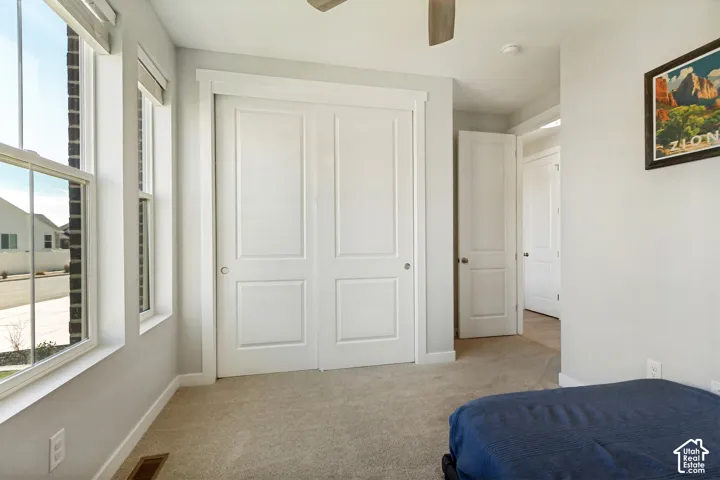 Dual pane windows, white paneled bifold closet doors, light neutral carpeting, and a ceiling fan