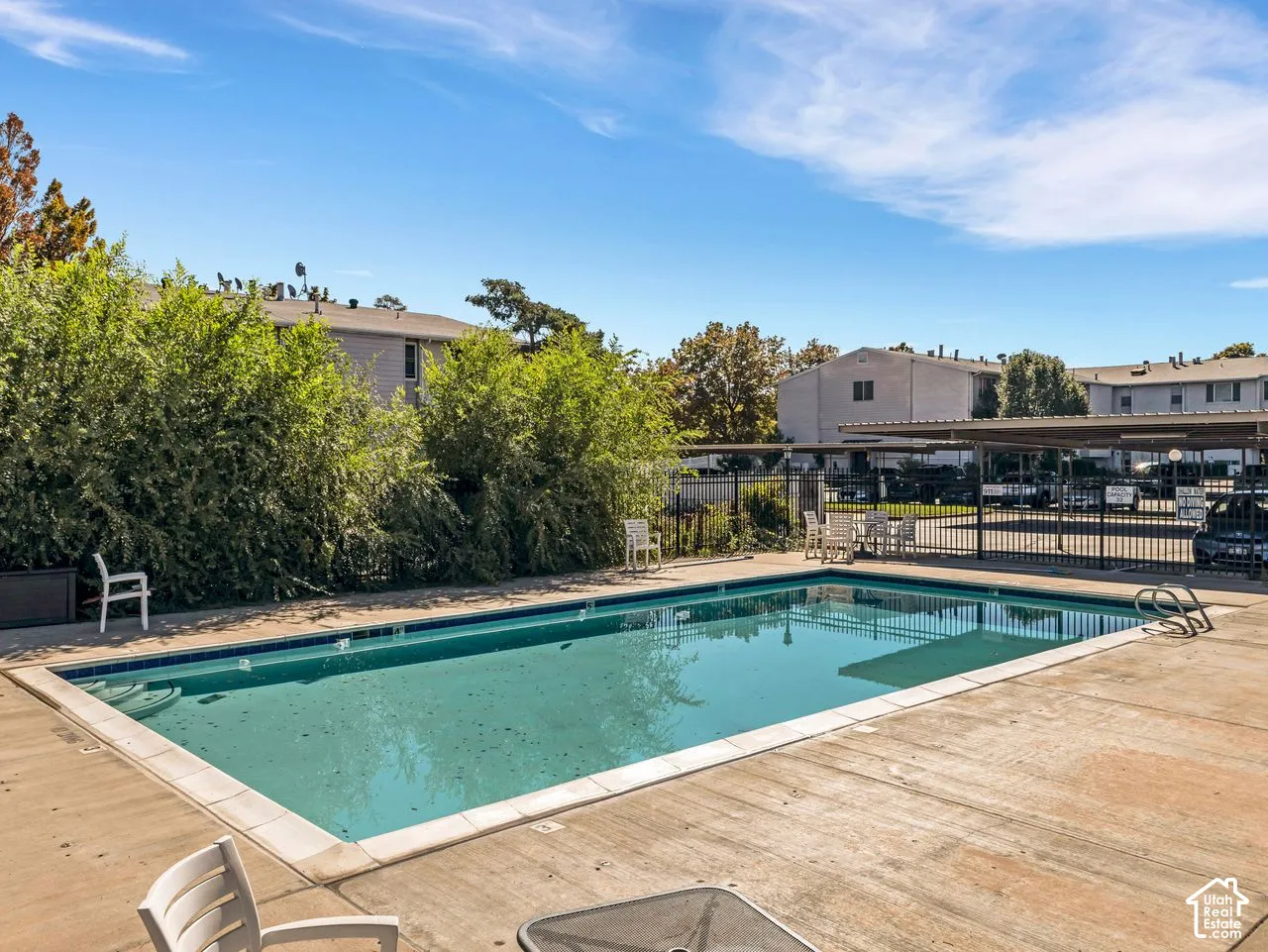 Outdoor swimming pool with concrete decking, surrounding mature landscaping, and an adjacent covered parking structure