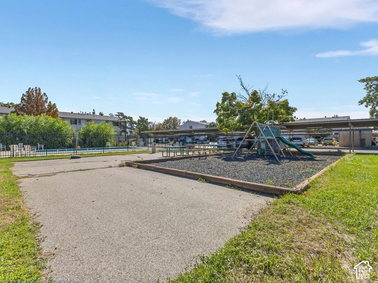 Playground area with a slide and climbing structure, an adjacent swimming pool, and covered parking structures