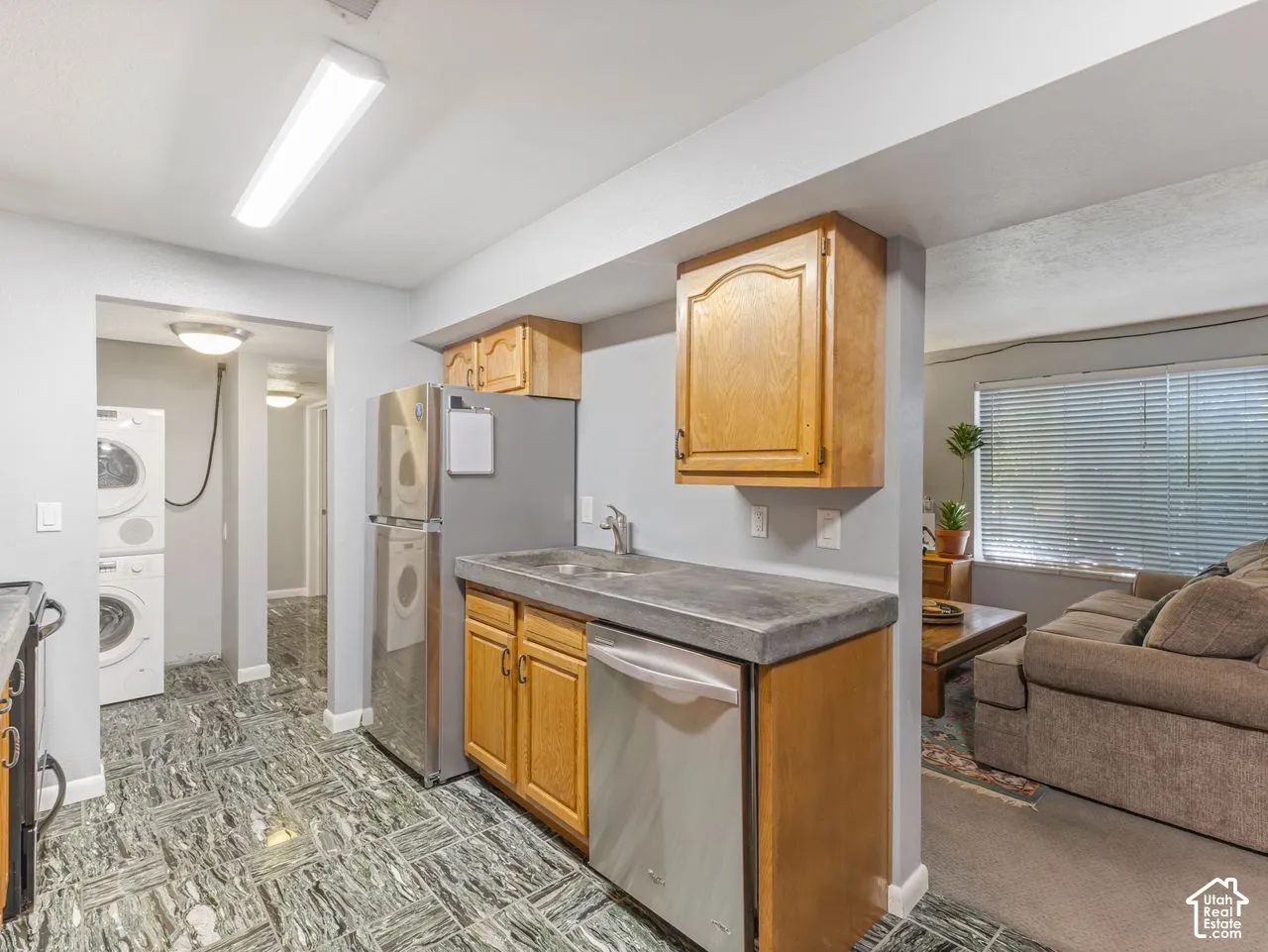 Kitchenette featuring wood cabinetry, stainless steel refrigerator, dishwasher, and a concrete-finish countertop with an integrated sink