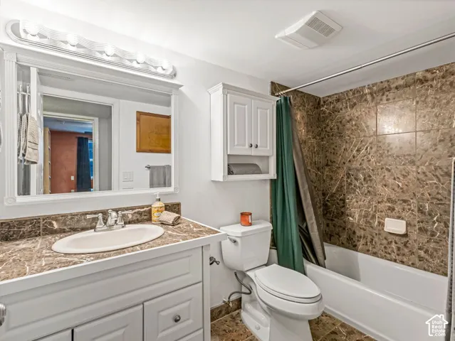 Bathroom featuring a white vanity with an undermount sink, a stone-finish countertop, and a vanity mirror with an overhead light fixture