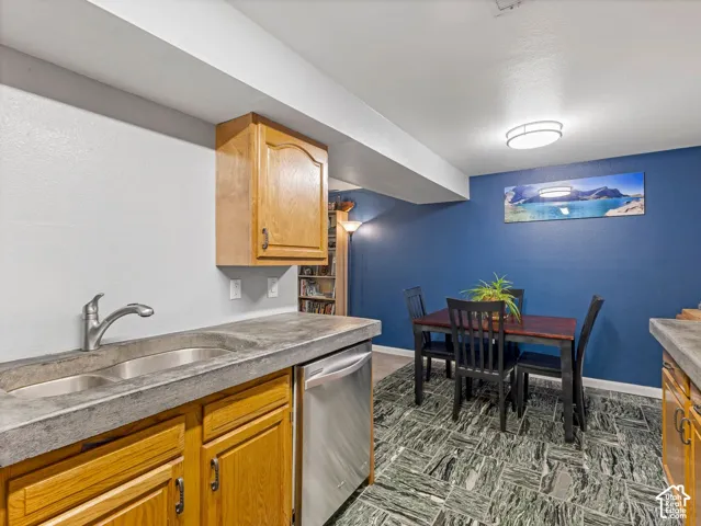 Concrete-finish countertops featuring an undermount double-basin sink and stainless steel faucet, wood cabinetry, a built-in dishwasher, and a patterned floor tile