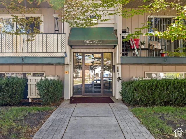 Entryway featuring a green awning, glass double doors, and a concrete pathway with brick accents