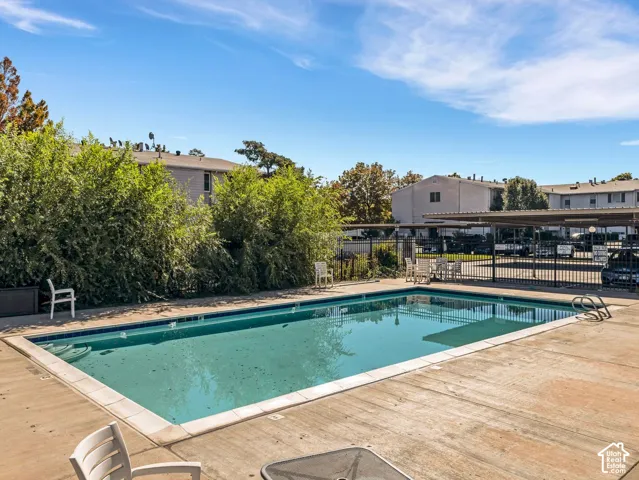 Outdoor swimming pool with concrete decking, surrounding mature landscaping, and an adjacent covered parking structure