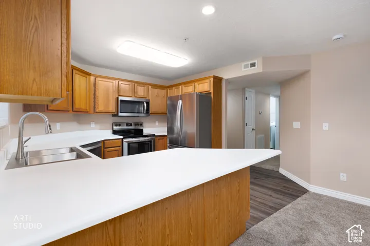 Kitchen featuring wood cabinetry, white countertops, stainless steel appliances, and an undermount sink with a gooseneck faucet