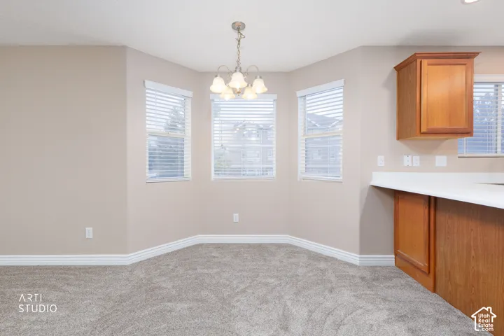 Carpeted dining nook with three windows, a ceiling-mounted chandelier, and integrated cabinetry with a white countertop