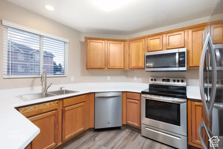 Wood-finish flooring, wood cabinetry, white countertops, stainless steel appliances, and a dual basin sink