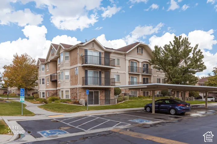 Multi-story building featuring balconies with black metal railings, stone veneer accents, and a covered parking structure