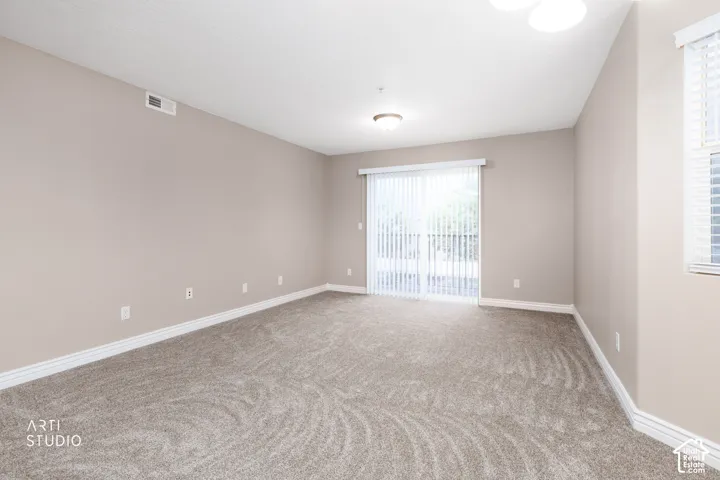 Neutral-toned walls, plush carpet, white trim, sliding glass door with vertical blinds, and ceiling-mounted lighting
