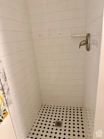 Shower stall with white subway tile walls, geometric mosaic floor tiles, a built-in shower shelf, and a wall-mounted shower fixture