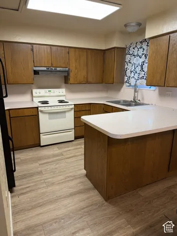 Kitchen featuring wood-finish cabinetry, white countertops, a built-in double basin sink, and wood-finish flooring
