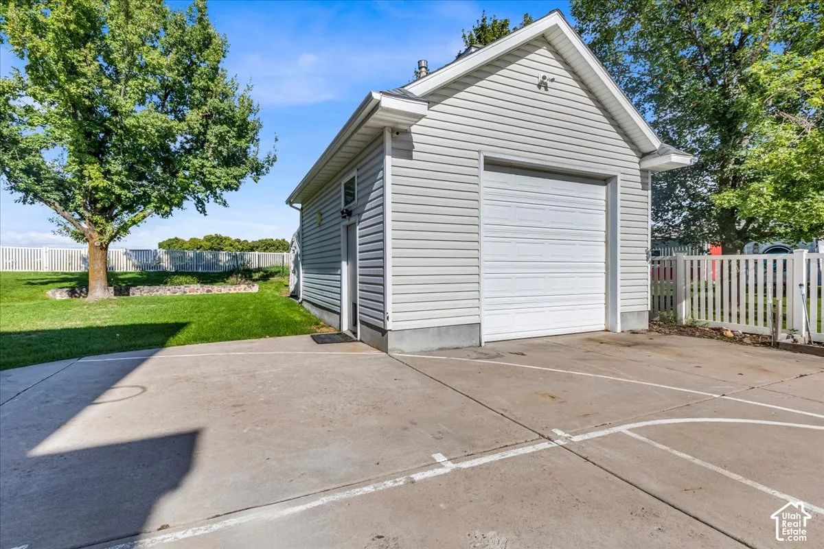 Detached garage with white siding and a roll-up door, concrete driveway, and a white picket fence