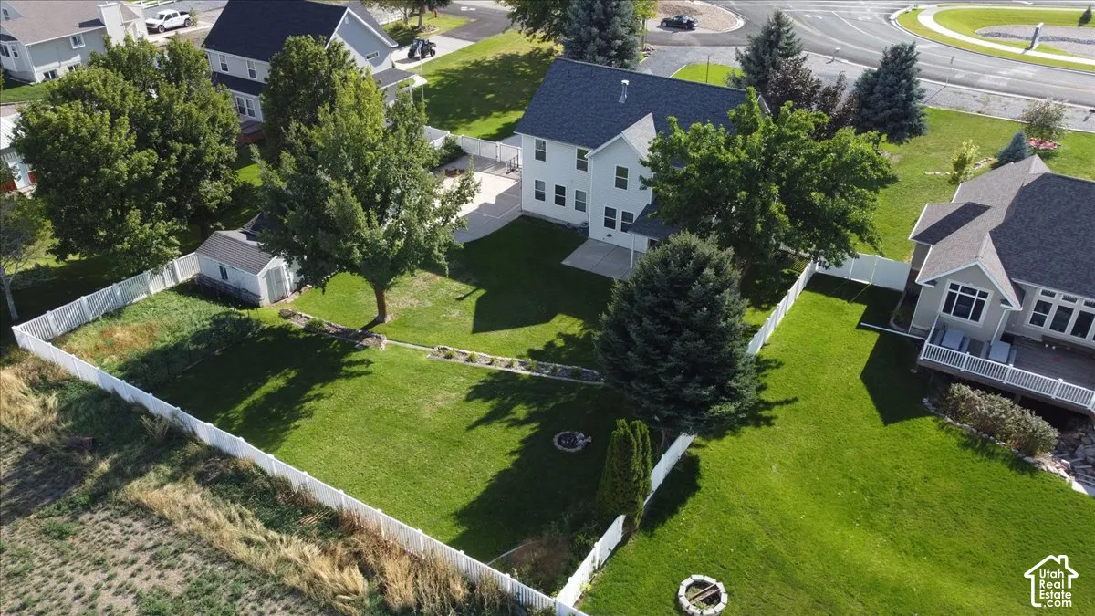 Expansive green lawn with a white privacy fence, mature trees, a detached storage shed, and a circular fire pit area
