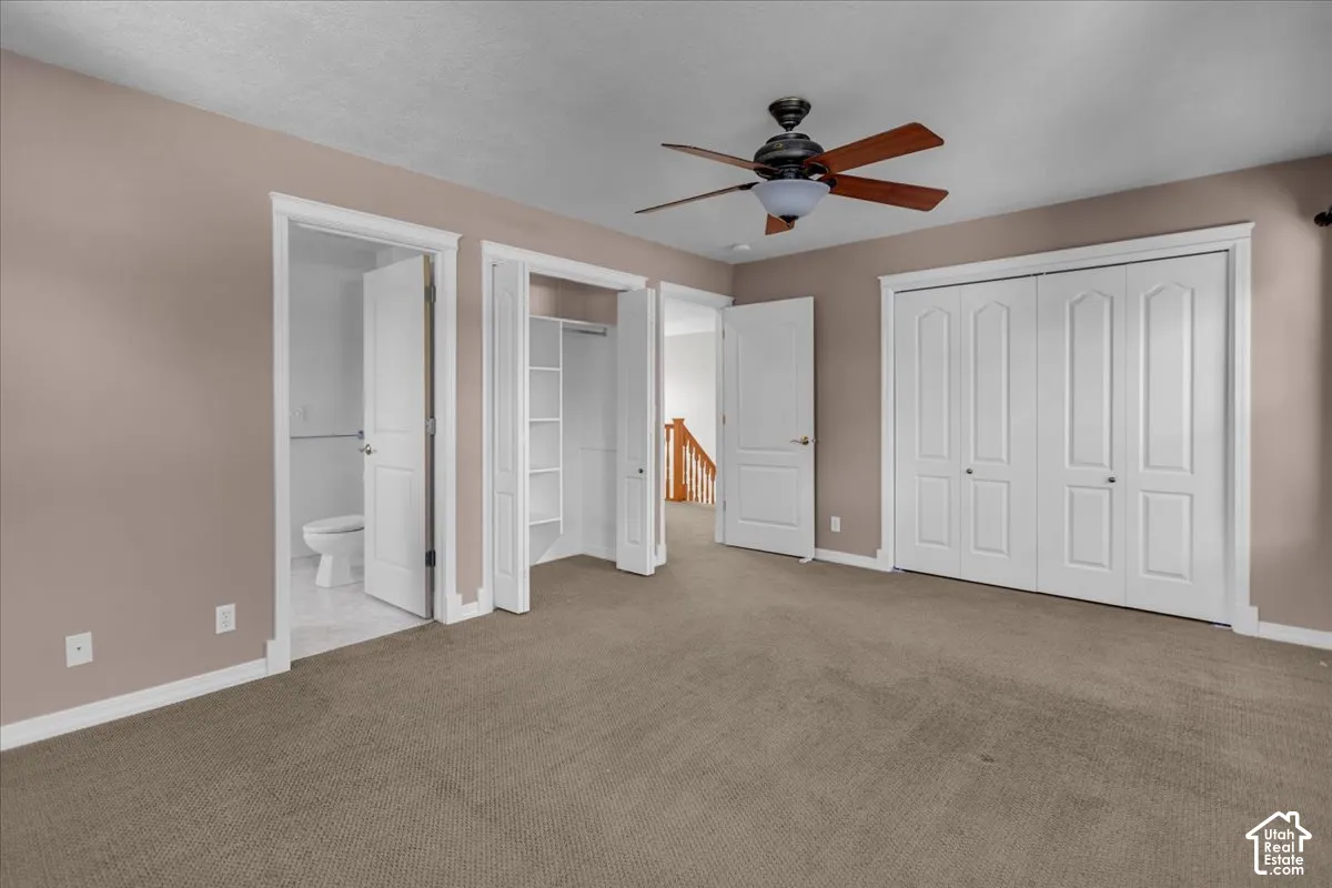 Primary Bedroom with a ceiling fan, two white bi-fold closets, and an adjacent bathroom with a toilet