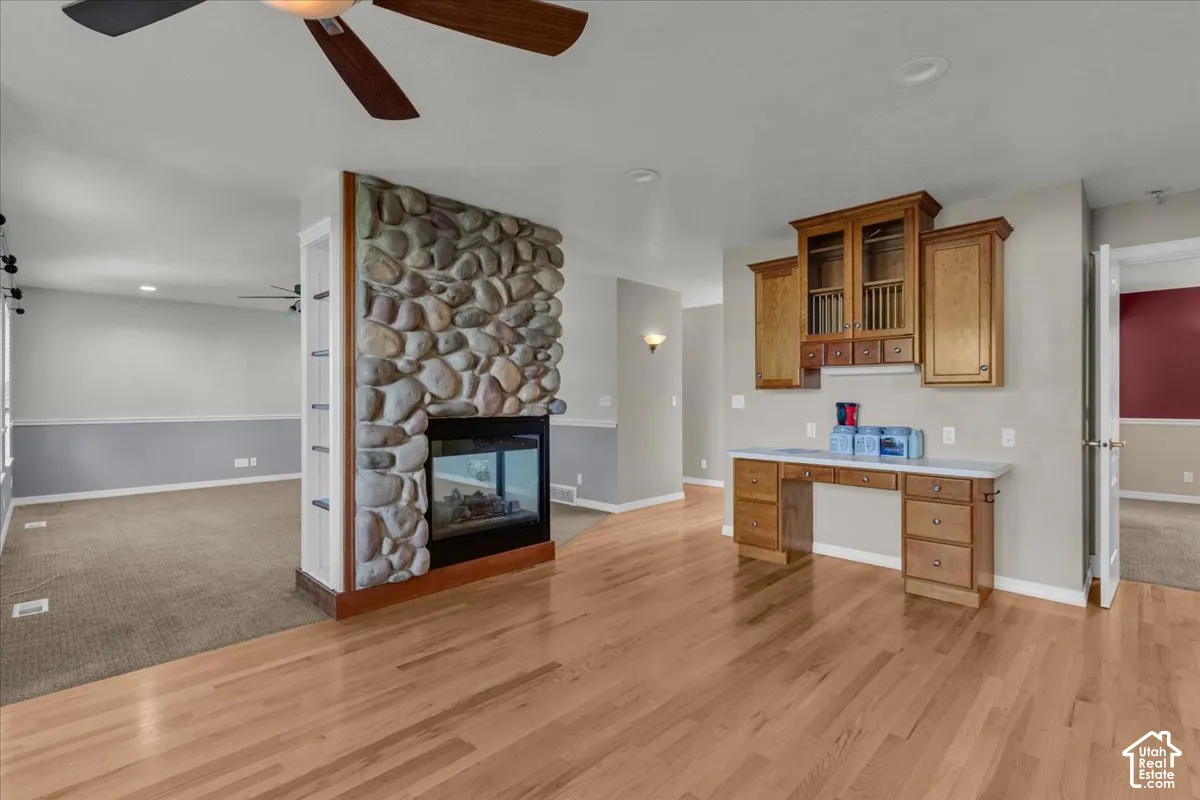 Hardwood flooring, stone-clad fireplace with glass-front insert, built-in desk with overhead cabinetry, ceiling fan with light fixture, recessed lighting