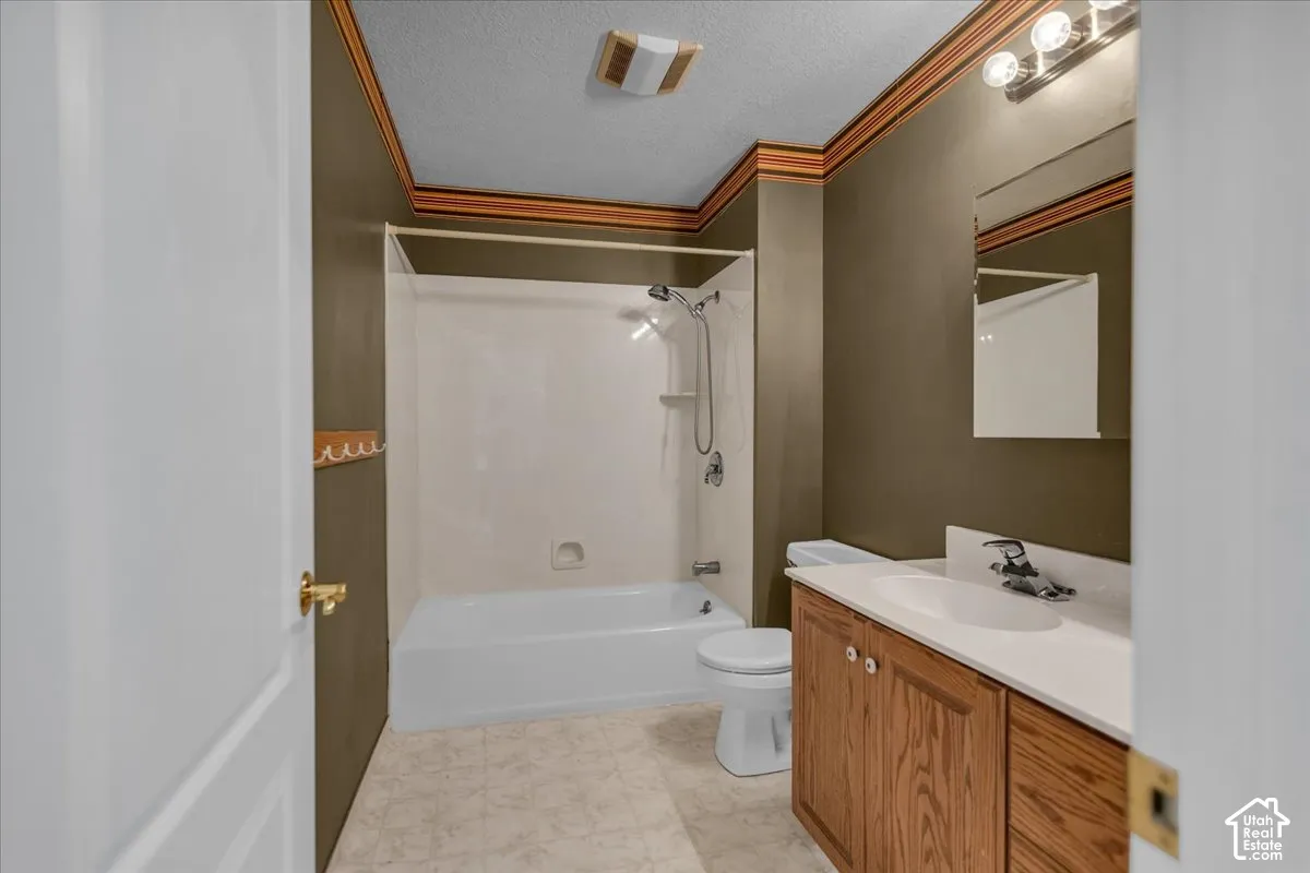White bathtub with shower, wood-finish vanity with integrated sink, wall-mounted mirror, and overhead lighting fixture