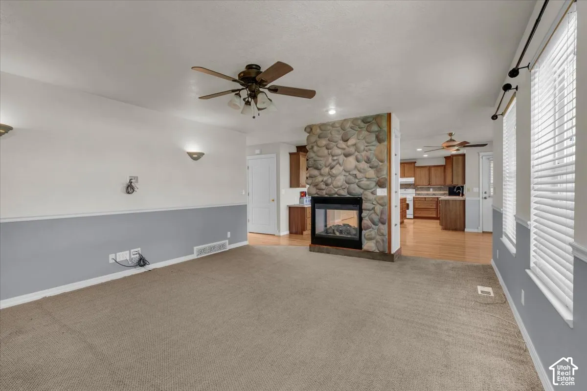 Living area featuring a stone-clad fireplace with a black hearth, ceiling fans, wall sconces, and natural light from horizontal blinds