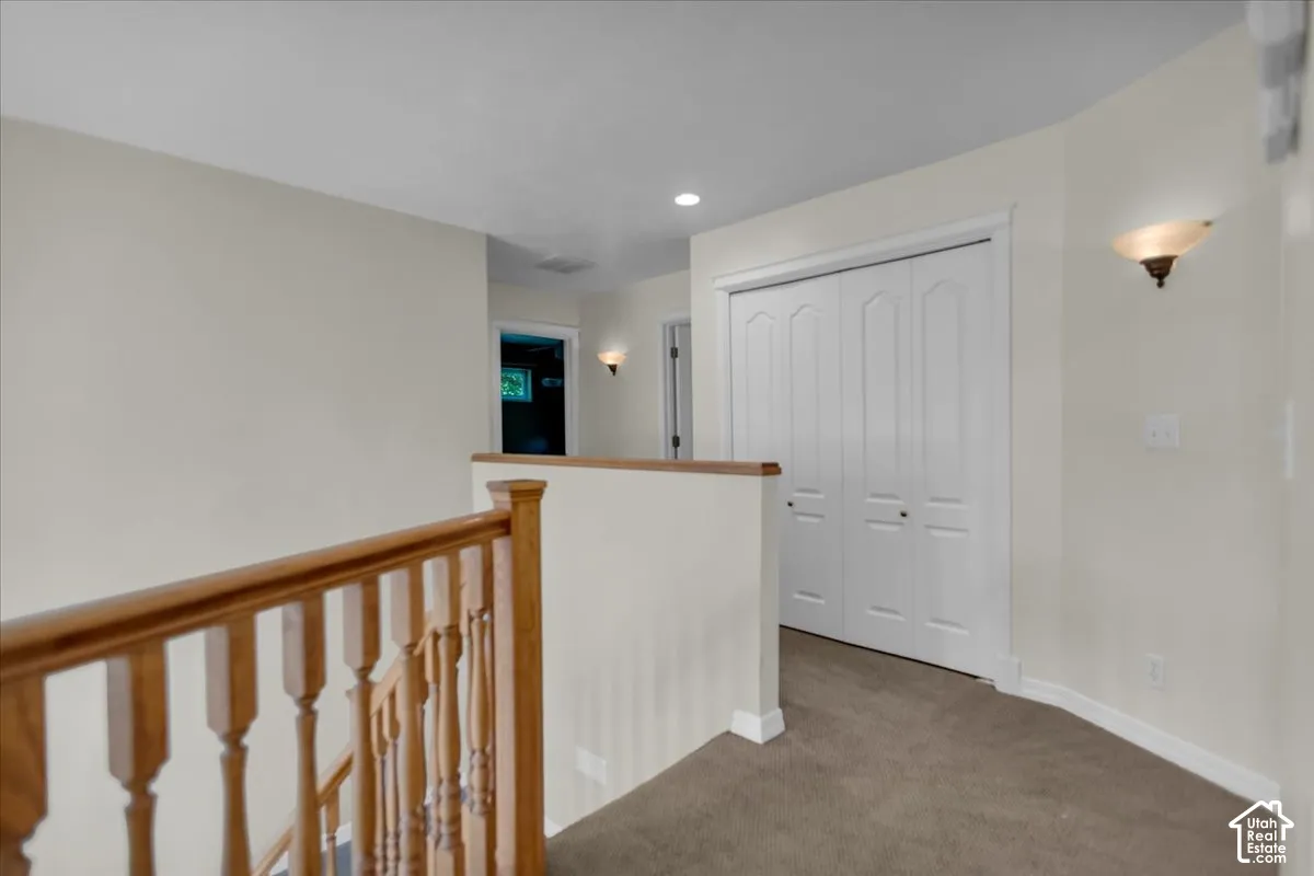 Carpeted hallway featuring a wooden banister, bi-fold closet doors, and wall sconces