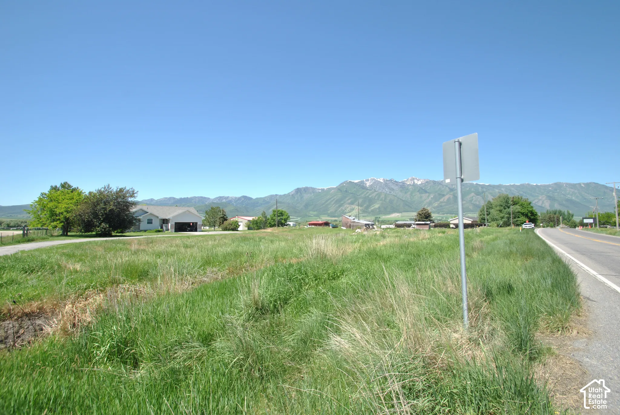 Secondary Lot - Expansive grass lot with a paved road, mountain range backdrop, and distant residential structures