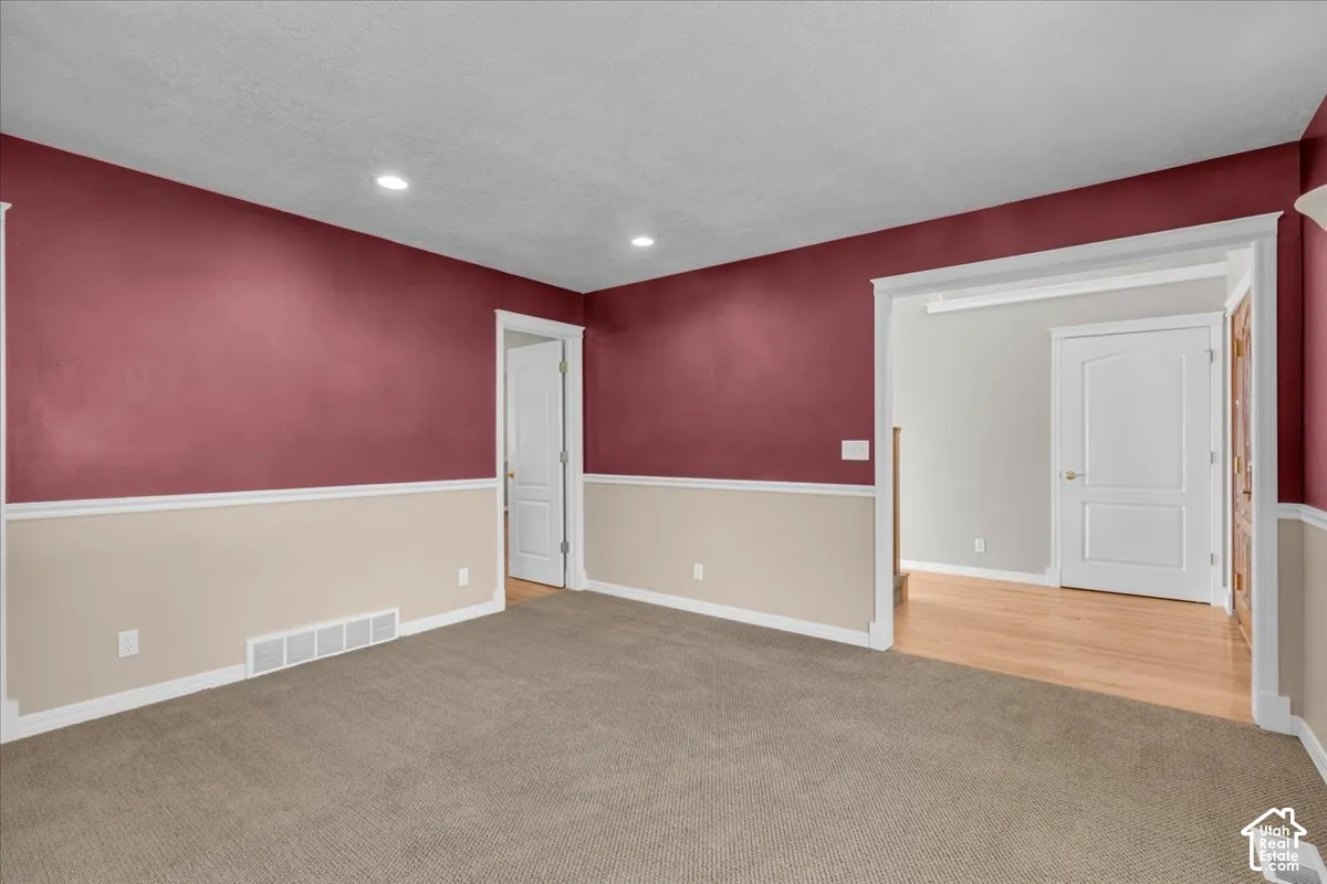 Recessed lighting, two-tone wall treatment, light wood-finish flooring, white paneled doors, and neutral carpeting.  Could be an office or living room.
