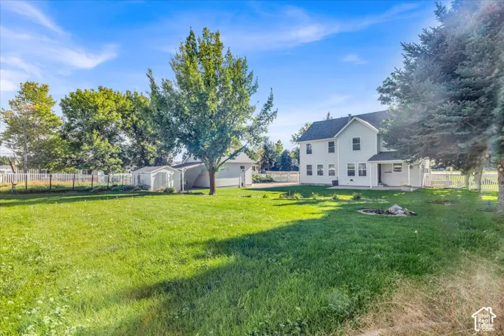 Expansive grassy yard with mature trees, white picket fencing, and a detached shed
