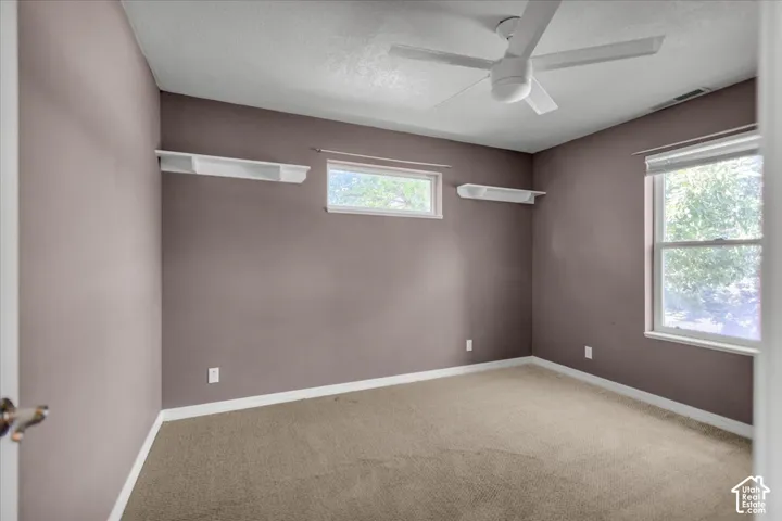 North East Bedroom with a Ceiling fan with light fixture, two windows, two built-in wall shelves, and neutral carpet flooring