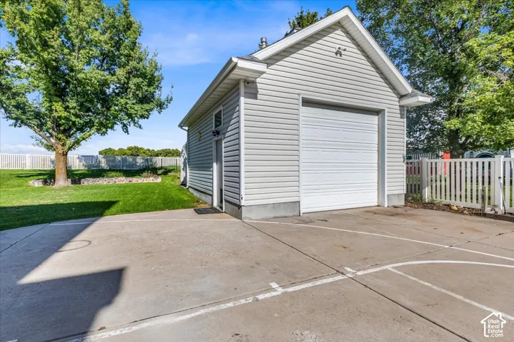 Detached garage with white siding and a roll-up door, concrete driveway, and a white picket fence