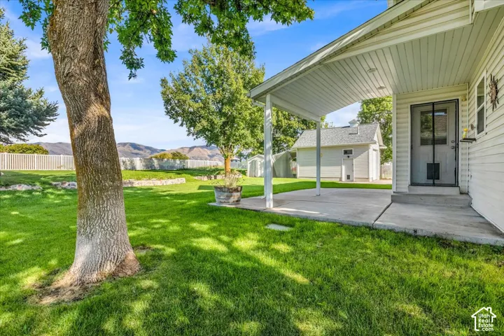 Expansive green lawn with mature trees, white privacy fencing, and a concrete patio with a covered awning