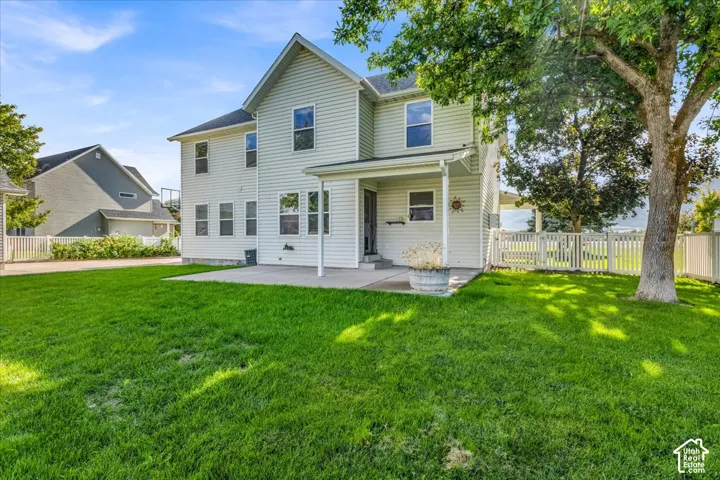 Expansive lawn area with a concrete patio, covered porch, and white picket fencing