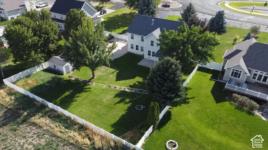 Expansive green lawn with a white privacy fence, mature trees, a detached storage shed, and a circular fire pit area
