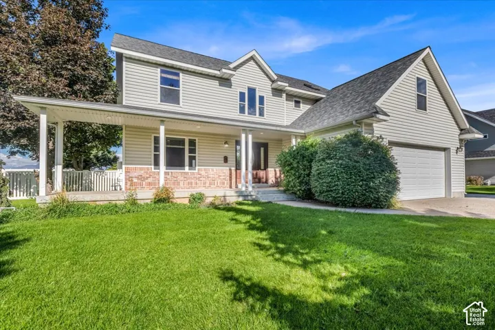 Two-story residence featuring a covered front porch, brick and siding exterior, attached garage, and a lush lawn