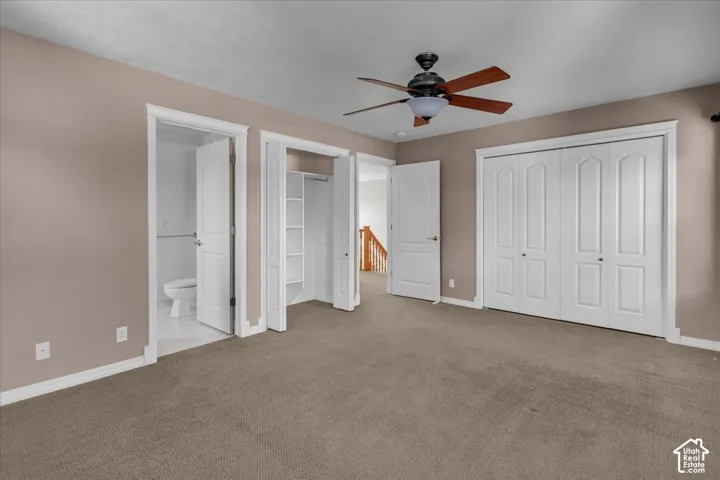Primary Bedroom with a ceiling fan, two white bi-fold closets, and an adjacent bathroom with a toilet