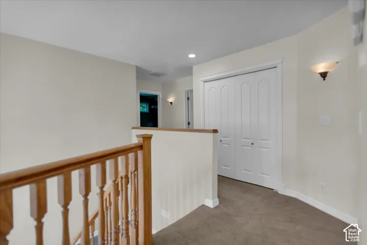 Carpeted hallway featuring a wooden banister, bi-fold closet doors, and wall sconces
