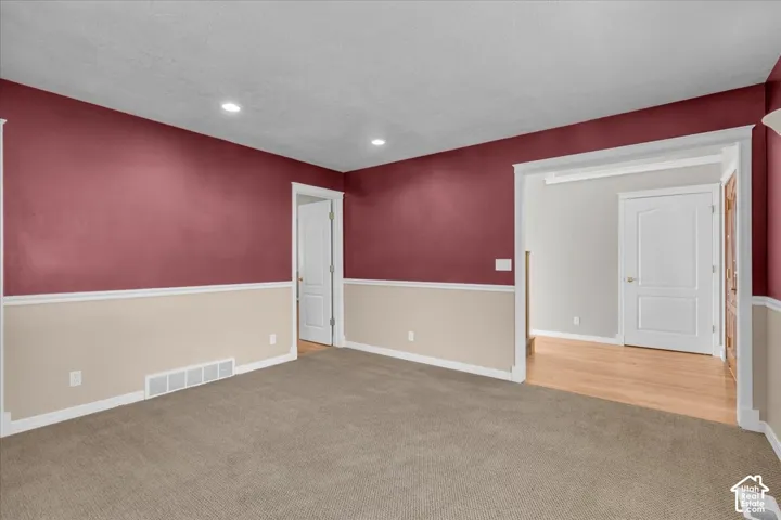 Recessed lighting, two-tone wall treatment, light wood-finish flooring, white paneled doors, and neutral carpeting.  Could be an office or living room.