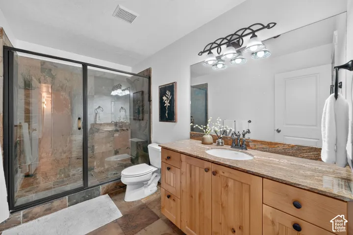 Glass-enclosed shower with stone tile surround, wood-finish vanity with countertop, oval sink, and large wall-mounted mirror
