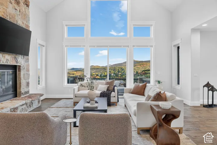 Great room with soaring ceilings, a stone fireplace, wood-finish flooring, and expansive windows