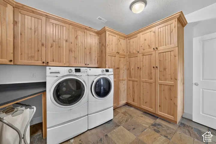 Extensive wood-finish cabinetry with crown molding, dark stone-finish countertops, and multi-toned stone tile flooring