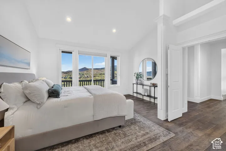 Vaulted ceiling with recessed lighting, expansive windows, wood-finish flooring, and a decorative column accent