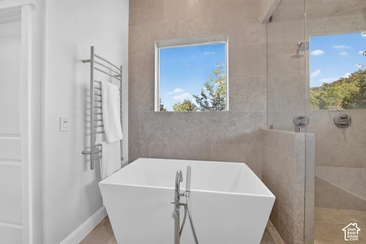 Freestanding soaking tub with floor-mounted faucet, walk-in shower with glass partition, and floor-to-ceiling tile surround
