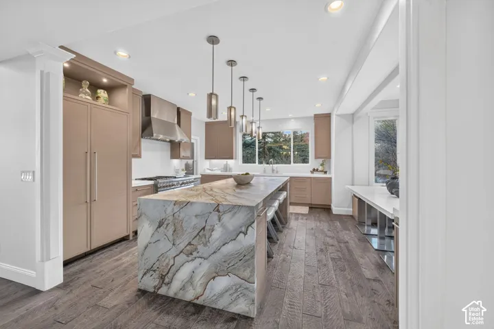 Waterfall island with a patterned countertop, wood-finish flooring, recessed lighting, built-in panel-ready refrigerator, and pendant lighting fixtures