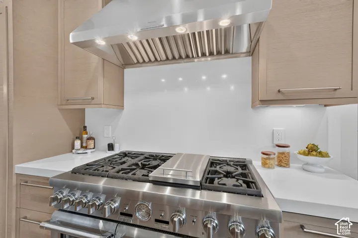 Stainless steel professional-grade range with a matching range hood, light wood-finish cabinetry, and white countertops