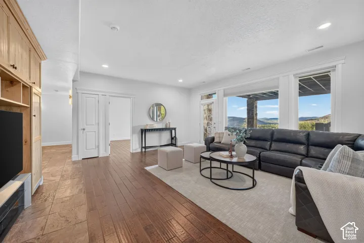 Spacious open-concept living area featuring wide-plank wood-finish flooring, recessed ceiling lighting, and expansive windows with natural light