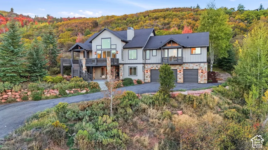 Contemporary mountain residence featuring multiple large windows, expansive exterior decking, a three-car garage, stone accents, and a sloped driveway
