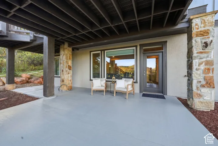 Lower-level patio with a painted concrete surface, stone-clad pillars, and exterior entry door with transom window