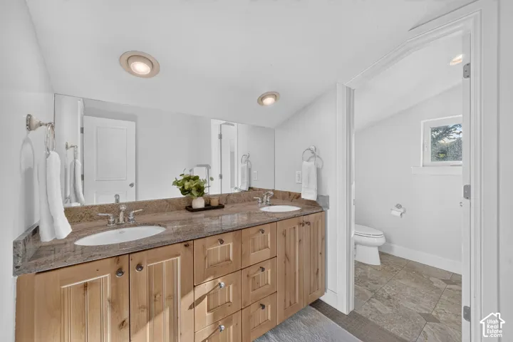 Double vanity with a granite countertop, recessed lighting, and wood-finish cabinetry